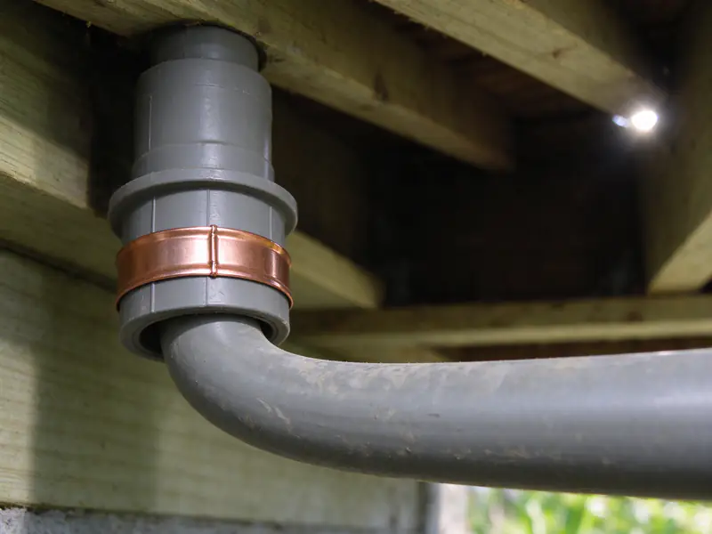 Close view of gray polybutylene pipe and a wide copper crimp band at a fitting